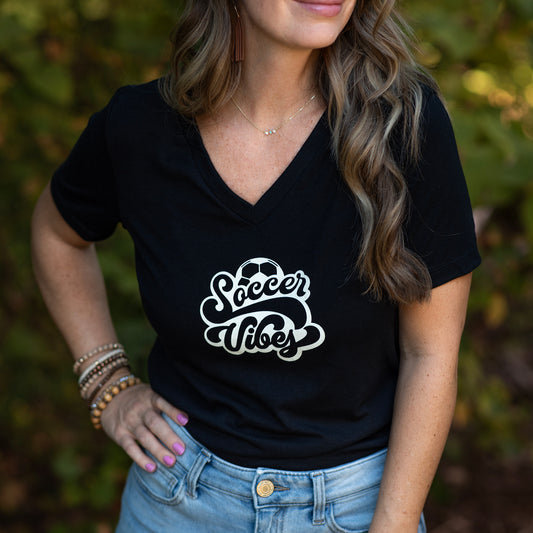 Person wearing a black t-shirt with 'Soccer Vibes' text, standing outdoors.