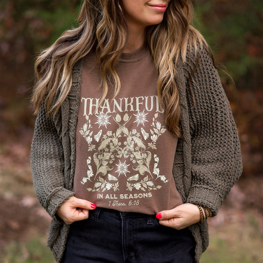 Woman wearing a brown 'Thankful in All Seasons' shirt outdoors