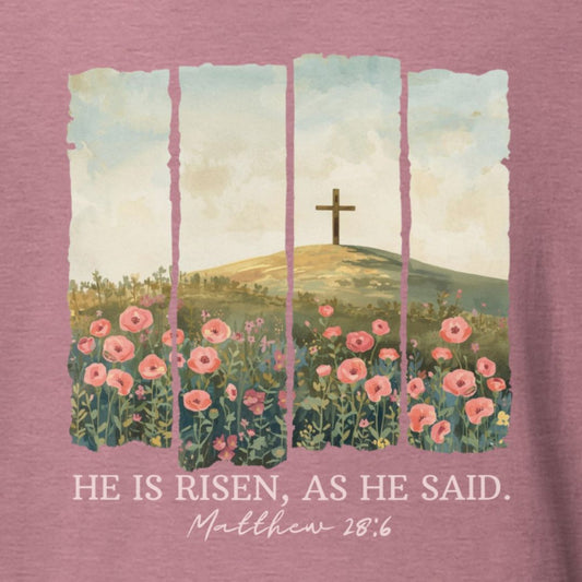 T-shirt with a cross and flowers design on a pink background, featuring the text 'He is risen, as he said. Matthew 28:6'.