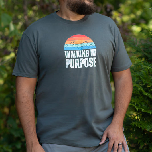 Person wearing a t-shirt with 'Walking in Purpose' text and a colorful design outdoors.