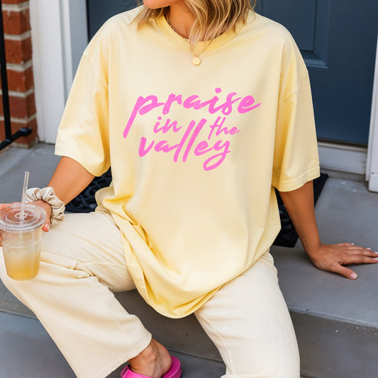 Person wearing a yellow oversized t-shirt with 'praise in the valley' text, sitting on a step.