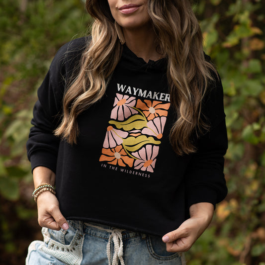 Person wearing a black crop hoodie with a colorful graphic and Waymaker In the Wilderness text in a natural setting