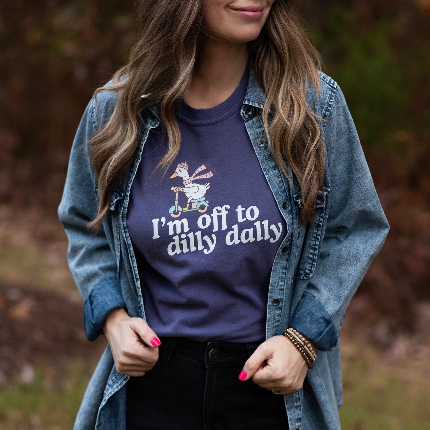 Woman wearing a purple t-shirt with text and a graphic, standing outdoors.
