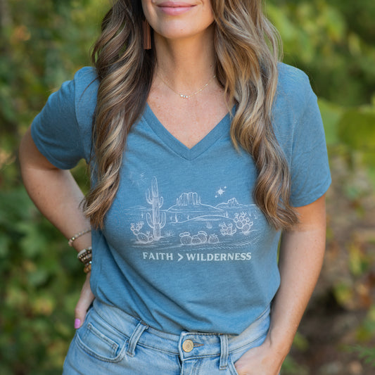 Minimalist t-shirt on model with a cactus and bold text reading "FAITH > WILDERNESS" — a spiritual, nature-inspired design symbolizing strength and serenity.