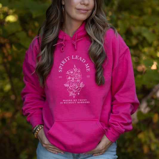Person wearing a pink hoodie with  Spirit Lead Me text and floral design outdoors.