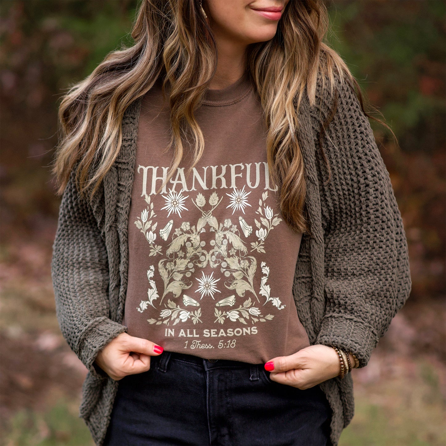 Woman wearing a brown 'Thankful in All Seasons' shirt outdoors