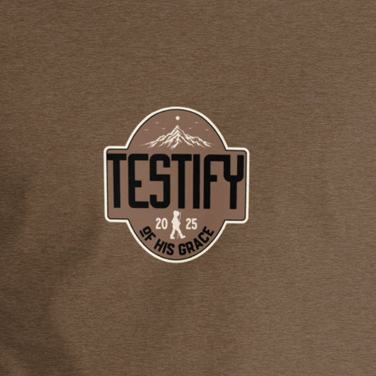Brown shirt with Testify of His Grace text with a mountain in the background. 