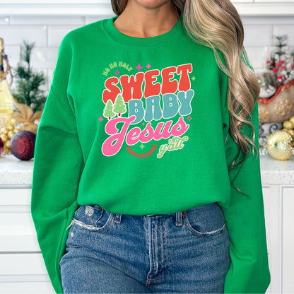 Green Christmas sweatshirt with retro-style text that reads ‘Ho Ho Holy—Sweet Baby Jesus Y’all’ in red, teal, and pink lettering, worn by a woman in a holiday kitchen setting.
