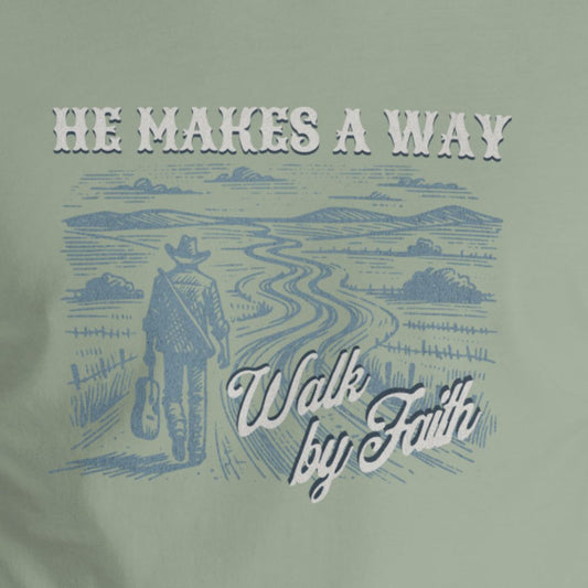 T-shirt with a graphic of a person walking on a path with text 'He Makes A Way, Walk by Faith' on a green background.