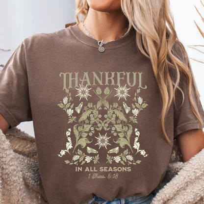 Person wearing a brown t-shirt with 'Thankful in All Seasons' design and floral elements.