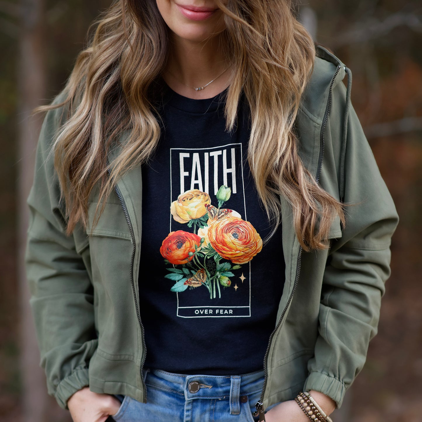 Person wearing a black t-shirt with floral design and 'FAITH OVER FEAR' text, paired with an olive green jacket.