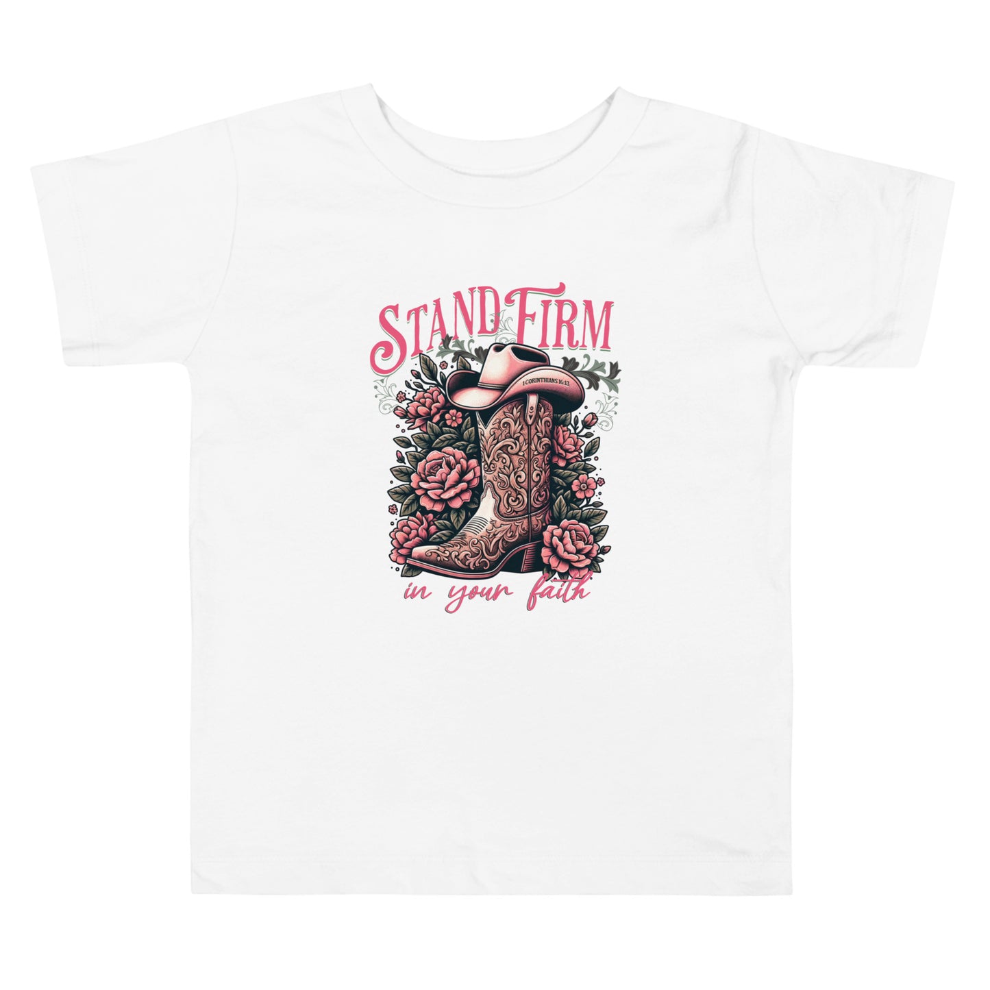Christian graphic tee featuring a cowboy boot and floral design with the inspirational phrase “Stand Firm in Your Faith” on a pink background. Includes Bible verse 1 Corinthians 16:13 inscribed on the hat. Faith-based western apparel on white t-shirt.