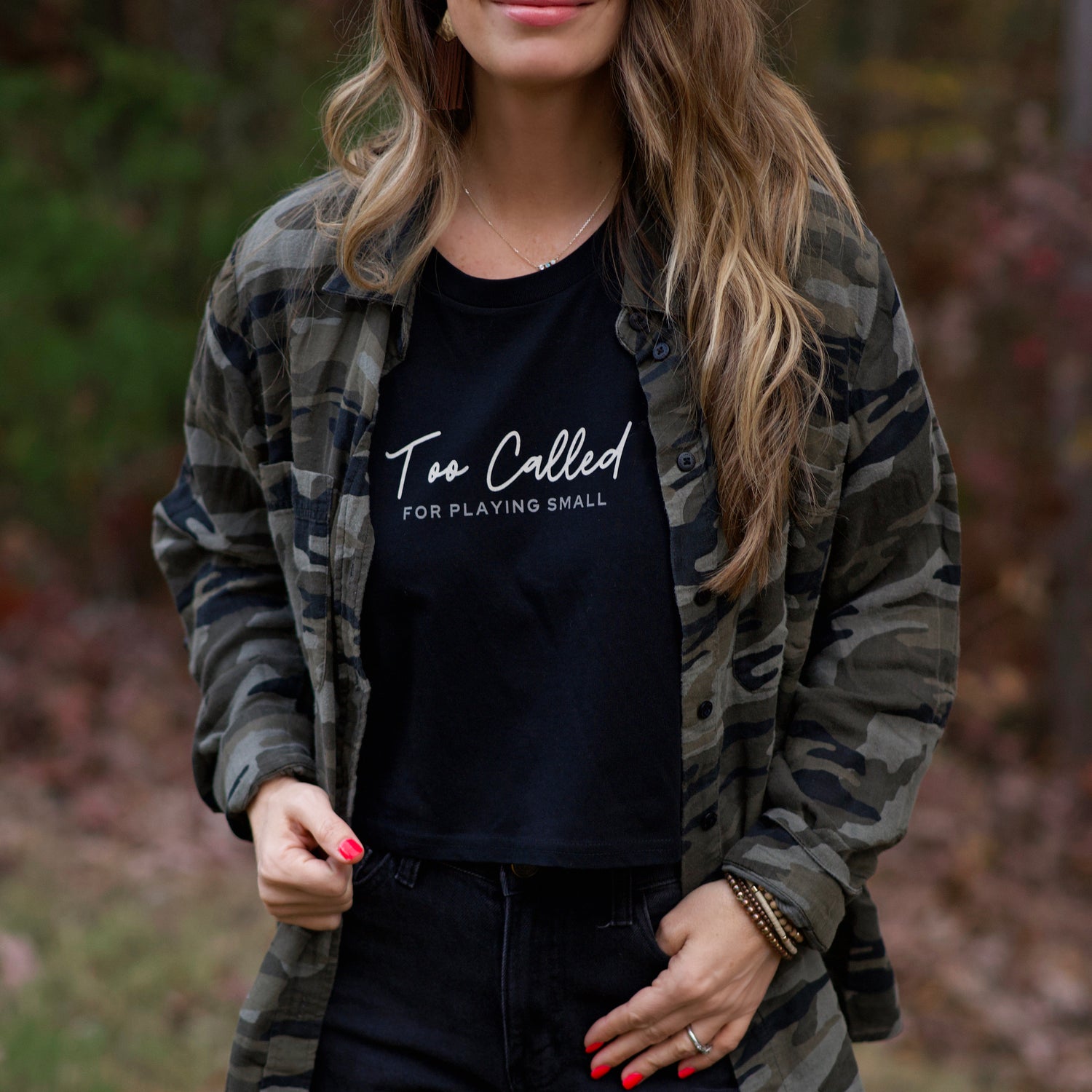 Woman wearing a black t-shirt with text and a camouflage jacket outdoors