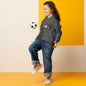A girl wearing the cool ducks hoodie is bouncing a soccer ball off of her knee.